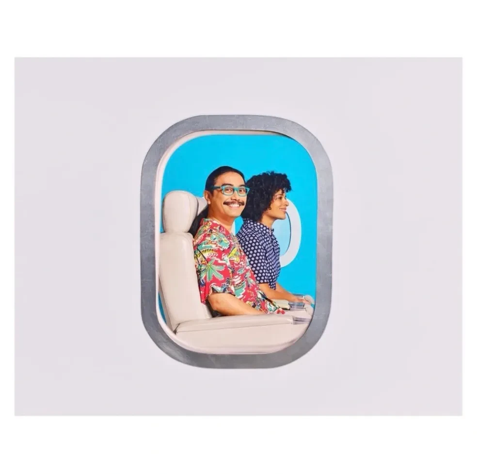 Two people in airplane window, bright blue background