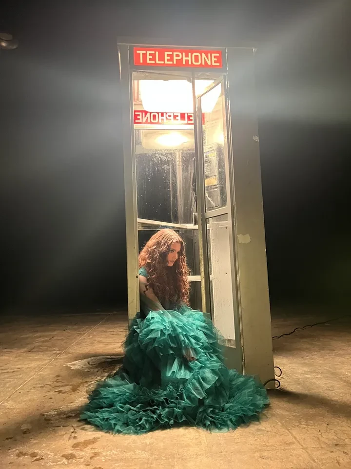 Woman in teal gown at vintage telephone booth